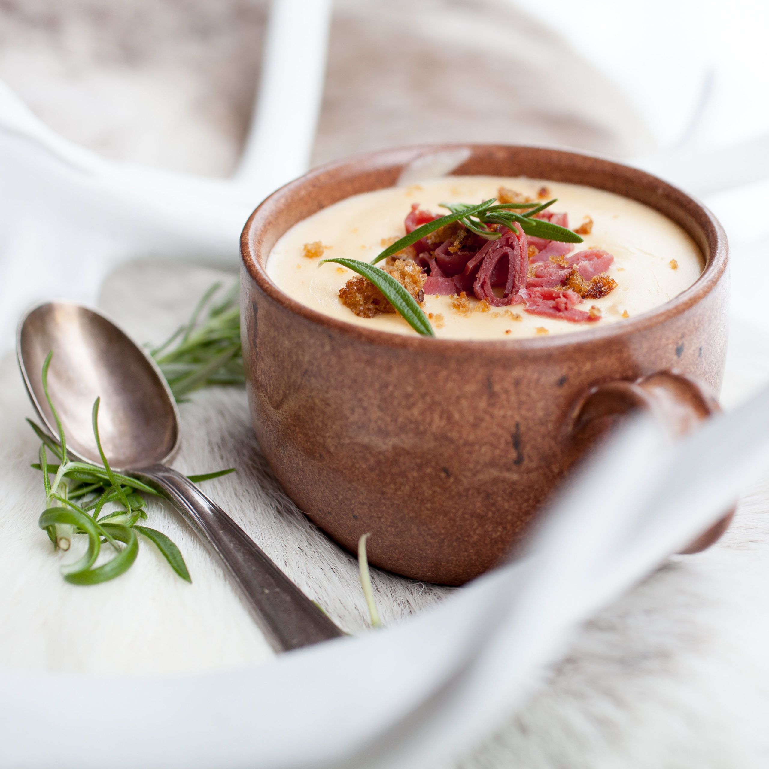 Suppe i kopp med speket reinsdyrkjøtt som topping. Dandert på reinsdyrskinn. Reinsdyrhorn rundt. 